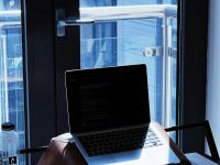 A laptop sits on a desk near a window. windows task manager, background processes, office pop up