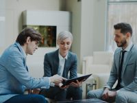 Three professionals discussing a tablet in a modern office. happy real estate team, property sales meeting, crm results graph