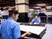 Factory workers folding fabric inside a garment factory. factory floor small business manufacturing software dashboard laptop
