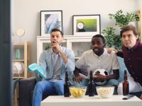 Best Sites Like 720pStream for Live Sports Streaming (2026) three men sitting on a couch in a living room live football match streaming, smart tv sports app, HD video playback screen