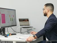a man sitting at a desk with a laptop and a computer modern office dashboard analytics screen team collaboration