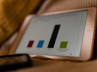 a tablet computer sitting on top of a bed financial charts and graphs on screen, budgeting analytics dashboard, colorful expense pie chart