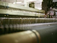 Close-up of threads on a large industrial loom. textile factory floor, industrial sewing machines, fabric rolls, production planning software dashboard