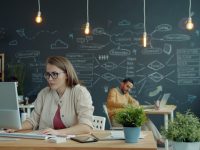 Woman working on computer in modern office with chalkboard. developer coding laptop database schema on screen modern workspace