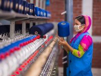 Woman working with blue yarn on a machine textile factory floor, industrial sewing machines, fabric rolls, production planning software dashboard